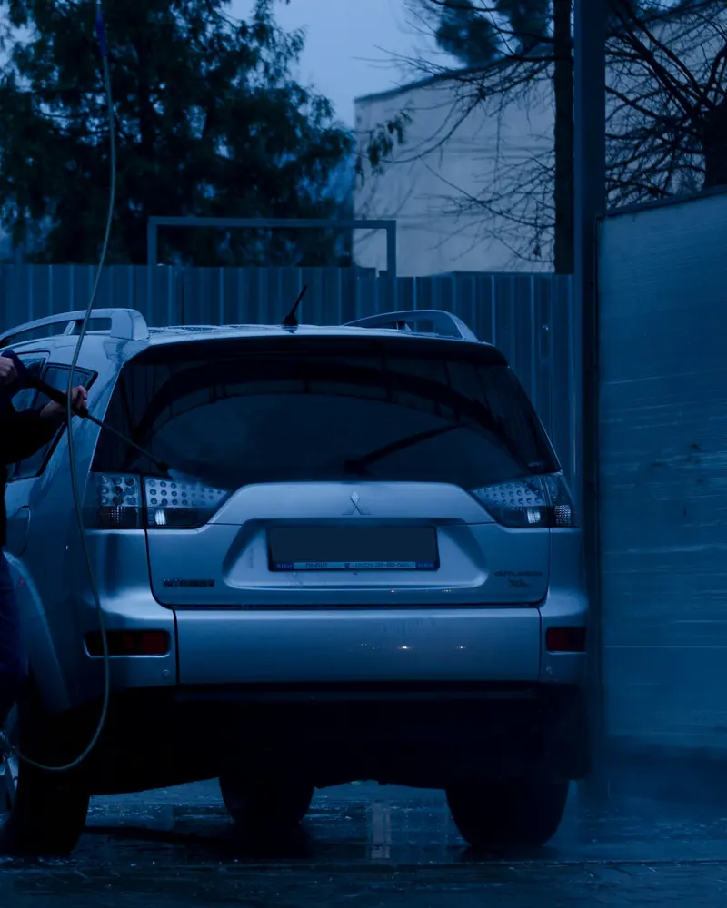 A man rinsing an SUV with a pressure wand in the evening