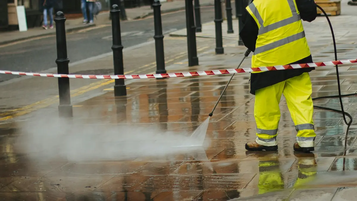 A worker pressure washing a paved walkway