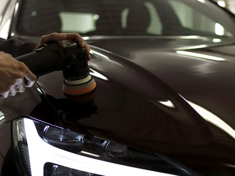 Hands guiding a machine polisher across black paint