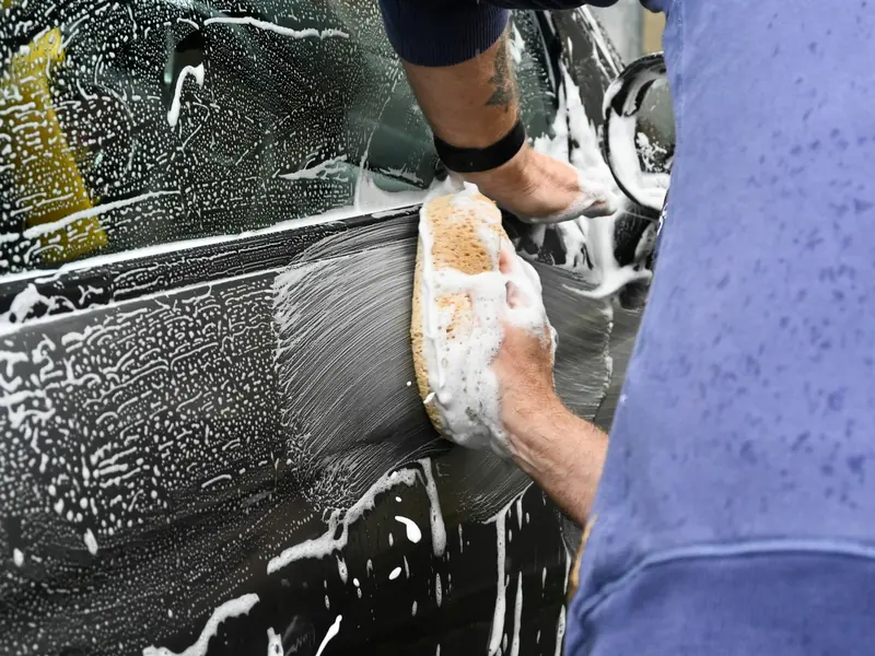 A gloved hand working a soapy sponge along a dark car door